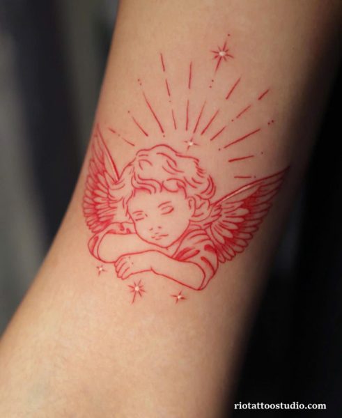 Red linework cherub angel tattoo with halo rays on wrist, minimalist cute angel tattoo