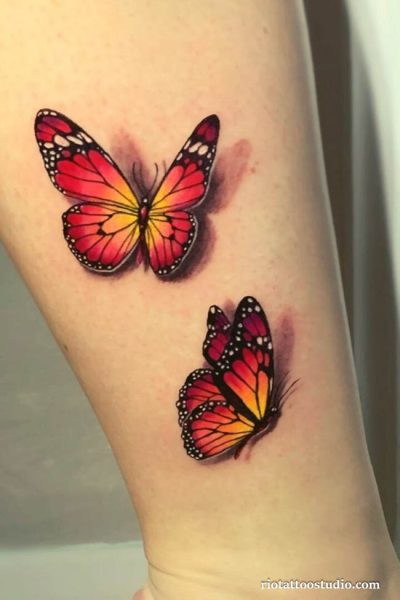 Two realistic monarch butterflies in red orange gradient with 3D shading on forearm, vibrant butterfly tattoo