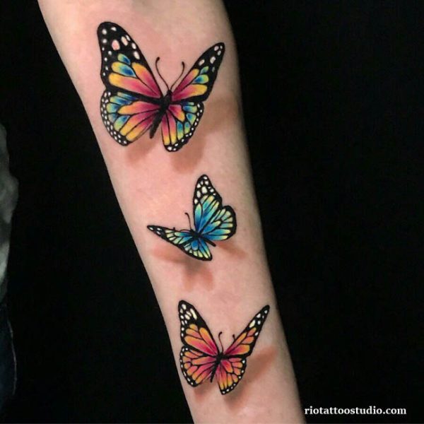 Three vibrant realistic butterflies in rainbow colors on forearm, colorful butterfly tattoo design