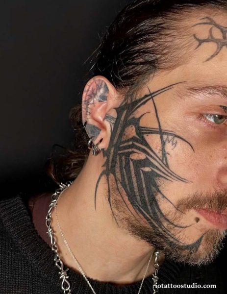 Gothic lettering TG face tattoo on temple side head, symbolic lettering face tattoo