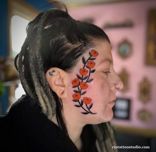 Orange flower chain face tattoo with leaves on side head temple, feminine bold face tattoo