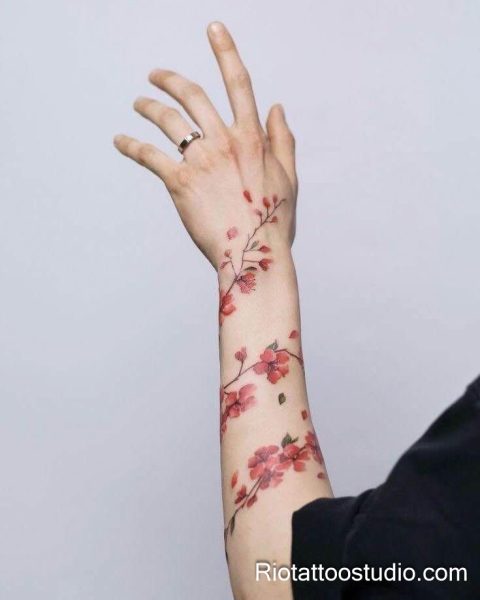 Red cherry blossom flowers trailing up hand and forearm, feminine sakura tattoo