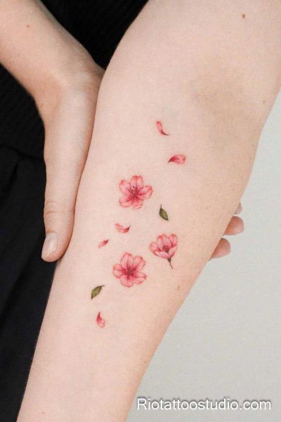 Watercolor cherry blossom petals falling along forearm, feminine sakura flower tattoo