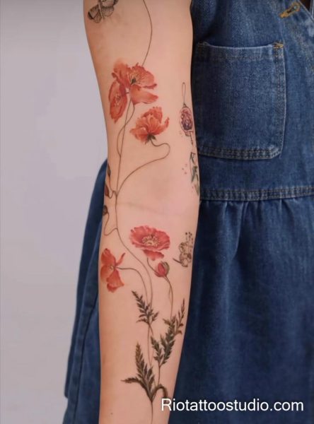 Watercolor red poppies with butterfly and greenery on forearm, artistic floral tattoo
