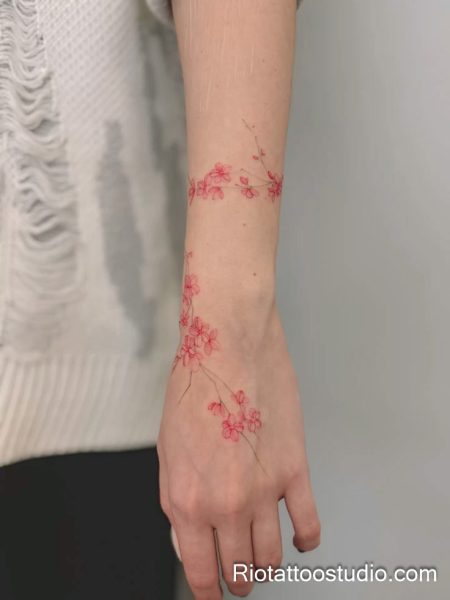 Thin pink cherry blossom branch wrapping forearm, minimalist sakura tattoo