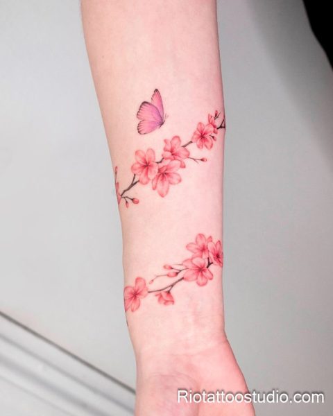 Pink cherry blossoms with purple butterfly on forearm, feminine sakura flower tattoo