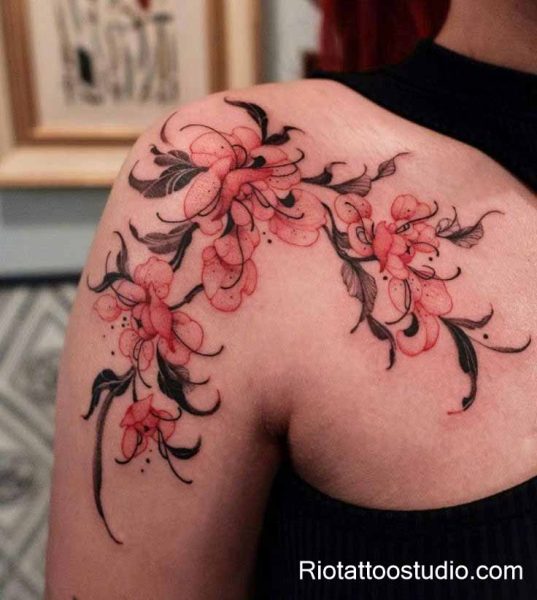 Delicate pink floral tattoo on shoulder with watercolor lilies and dark leaves, feminine flower tattoo for women