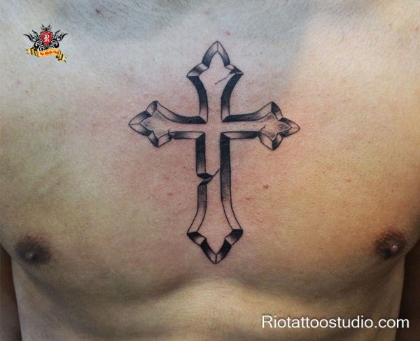 Large 3D cracked ornate cross tattoo centered on chest, bold black and grey shading with sharp fleur-de-lis edges, powerful chest cross tattoos for men symbolizing strength and resilience