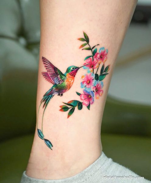 Large vibrant hummingbird tattoo with orange hibiscus flower on thigh, bold hummingbird tattoo design