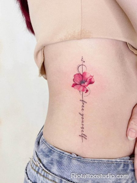 Small pink flower lotus tattoo with "free yourself" script on rib, minimalist lotus tattoo