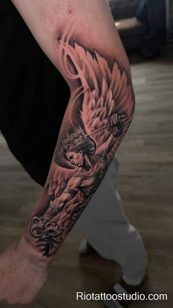 Archangel michael tattoo defeating demon with massive wings on arm, realistic religious tattoo