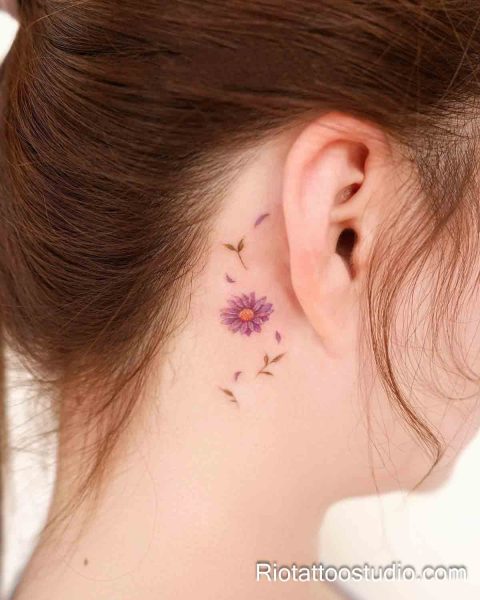 Small purple daisy flower behind the ear, minimalist behind-the-ear tattoo