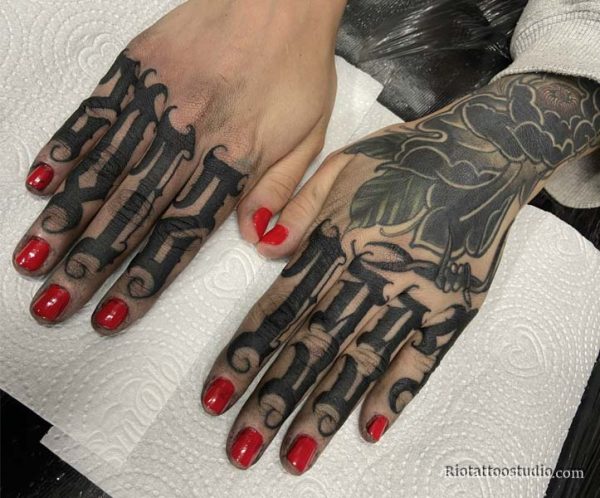 a large realistic peony tattoo on the back of the hand connected to elegant script lettering on the fingers