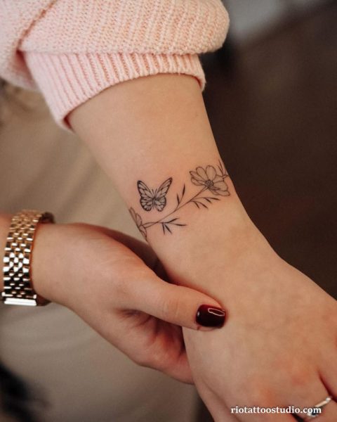 Butterfly and floral wrist tattoo in black linework on inner wrist, feminine wrist tattoo ideas