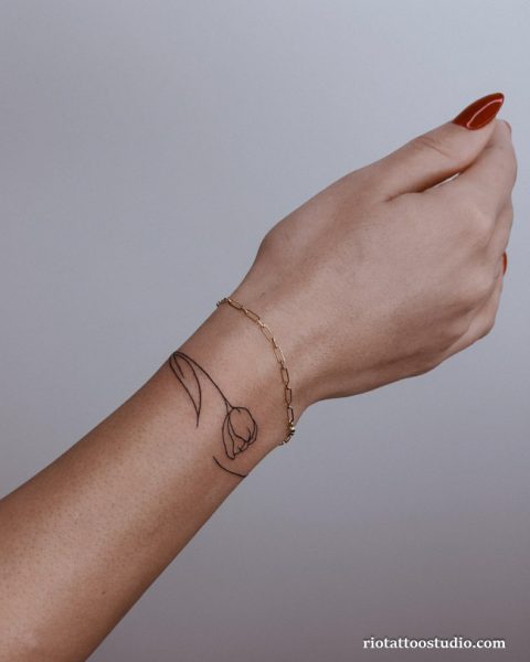 Minimal floral wrist tattoo with blue and red flowers on branch, small delicate wrist tattoo