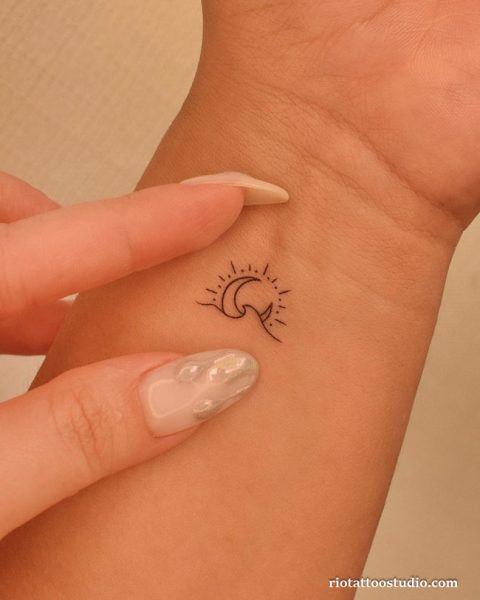 Minimal sun and crescent moon wrist tattoo in fine black linework, small meaningful wrist tattoo