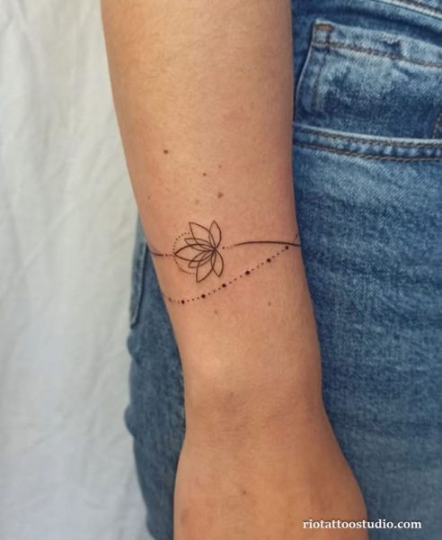 Minimal lotus flower wrist tattoo with dotted trail line, symbolic small wrist tattoo