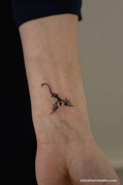 Minimalist dragon wrist tattoo in black fine line, small mythical wrist tattoo