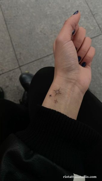 Minimal star cluster wrist tattoo in black linework with rays, tiny celestial wrist tattoo