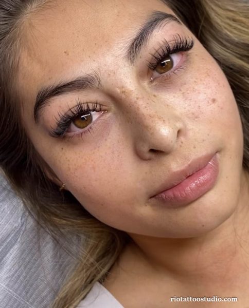 A trendy woman sporting a global freckles tattoo look, mirroring the popular sun-kissed aesthetic found in Western beauty trends.