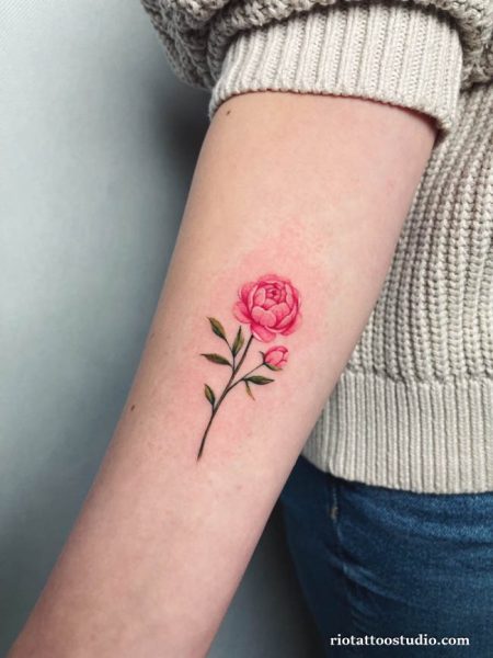 Small pink peony tattoo with stem and leaves on inner arm, minimalist peony tattoo ideas