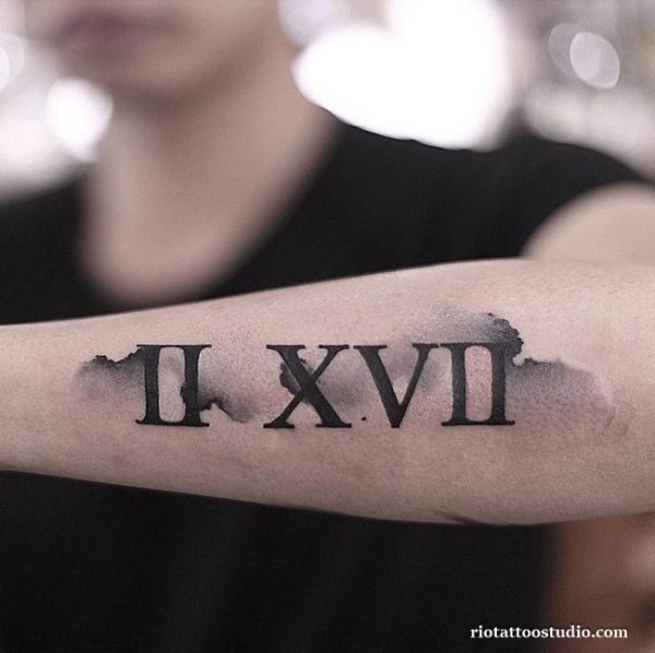Roman numeral tattoo II.XVII with ink splash effect on forearm, artistic roman letter tattoo ideas