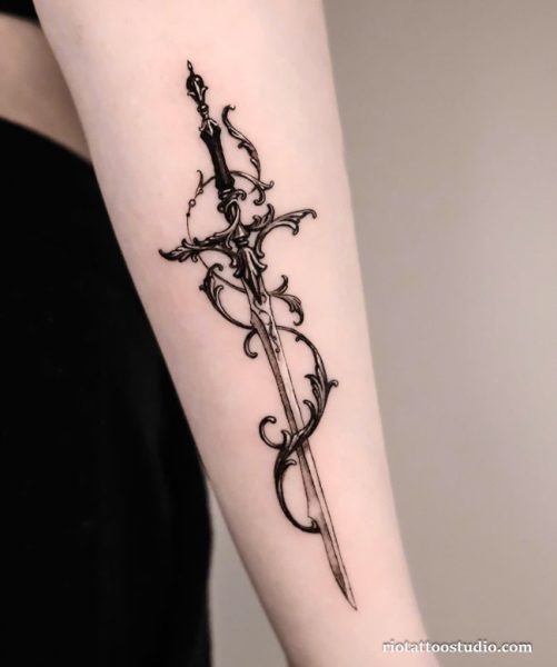 Ornate filigree sword tattoo with swirling vines on upper arm, elegant sword tattoo ideas
