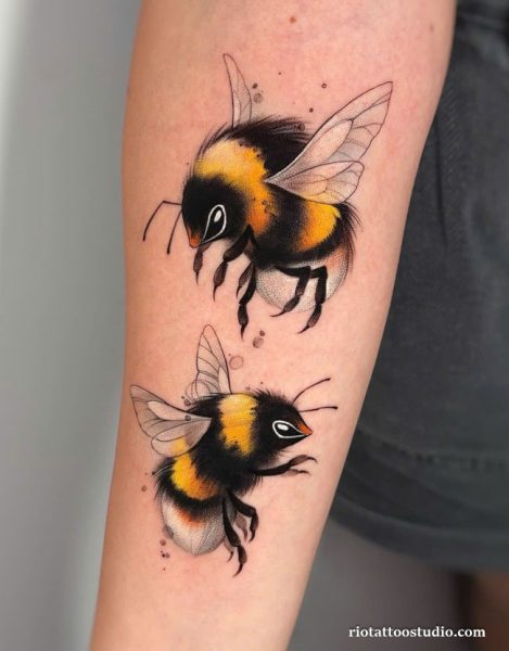 Two realistic bumblebees in flight tattoo with yellow and black coloring on arm