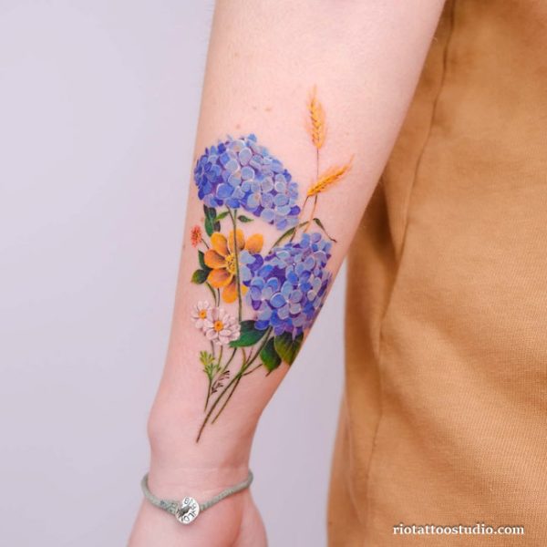 Colorful birth flower tattoo with blue hydrangea, yellow daisy and wheat on forearm, realistic birth flower tattoo ideas