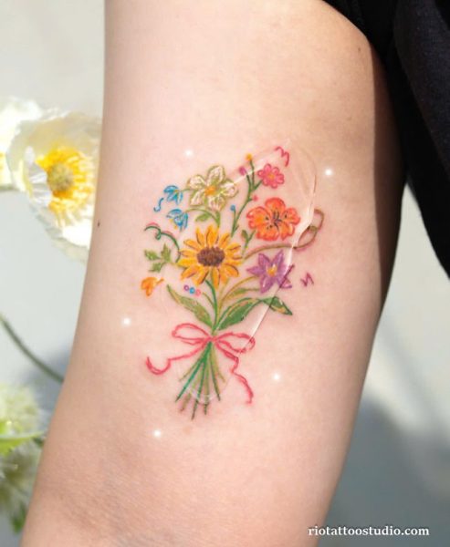 Colorful birth flower bouquet tattoo with sunflower and pink ribbon on upper arm, fresh birth flower tattoo ideas