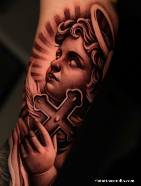 Chicano tattoo of angel with halo and cross on forearm, realistic black and grey chicano tattoo ideas