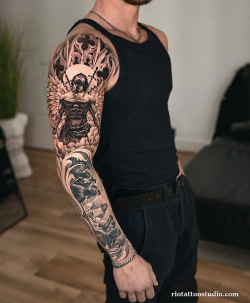Full sleeve chicano tattoo with Jesus on the cross, clouds, waves and sacred imagery on man’s arm