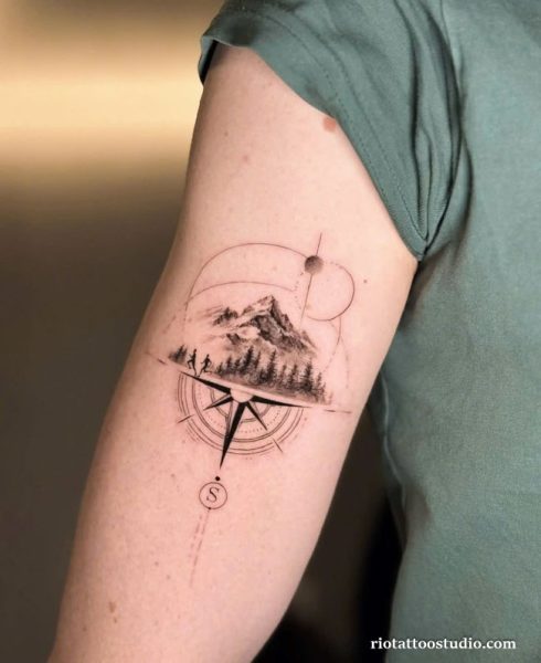 Minimalist geometric compass tattoo with mountain landscape and hikers on upper arm