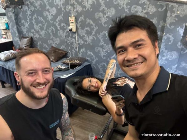 A happy foreign client smiling and posing with their new tattoo alongside a professional artist at Rio Tattoo Studio.