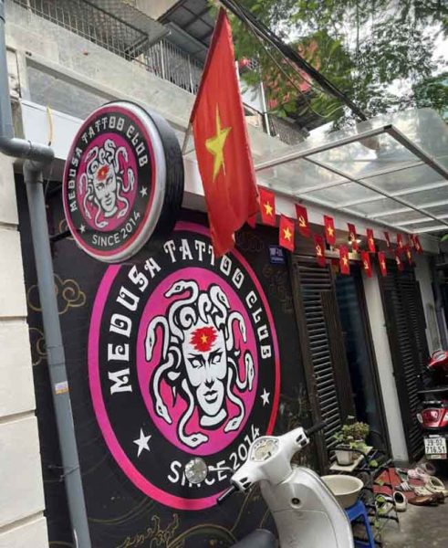 The distinctive round illuminated sign and main entrance of Medusa Tattoo Studio in Hanoi, Vietnam, featuring the bold pink Medusa logo and the Vietnamese flag