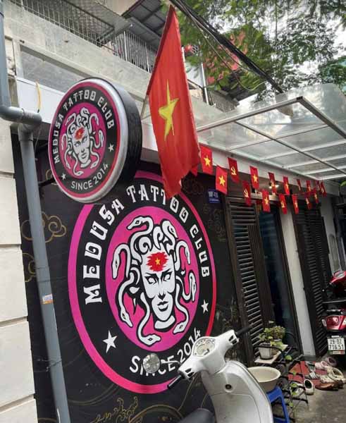 The distinctive round illuminated sign and main entrance of Medusa Tattoo Studio in Hanoi, Vietnam, featuring the bold pink Medusa logo and the Vietnamese flag