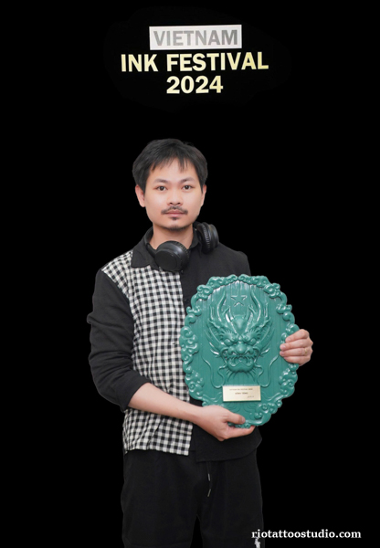 Award-winning tattoo artist from Rio Tattoo Studio holding a prestigious trophy and certificate at a tattoo convention.