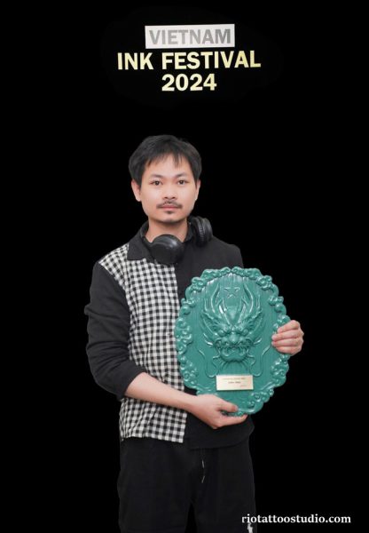 Award-winning tattoo artist from Rio Tattoo Studio holding a prestigious trophy and certificate at a tattoo convention.