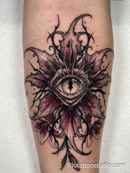 Dark floral evil eye tattoo with purple lily flowers and red gems on leg, evil eye tattoo ideas