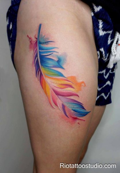 Rainbow watercolor feather tattoo on thigh with colorful splashes, bright feather tattoo ideas