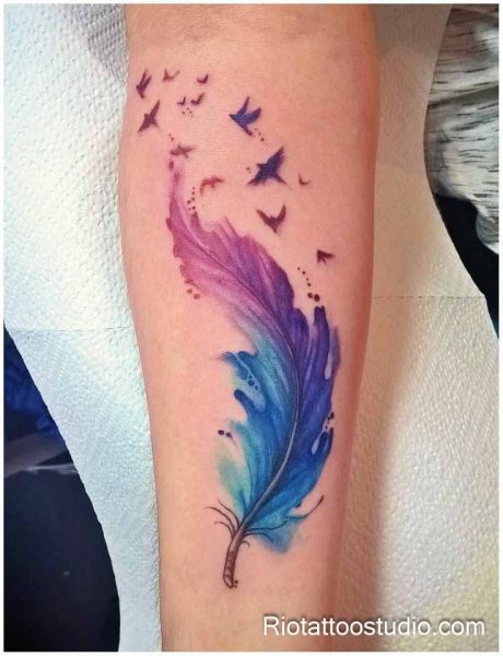 Watercolor feather tattoo in purple blue and pink with flying birds on arm, colorful feather tattoo ideas