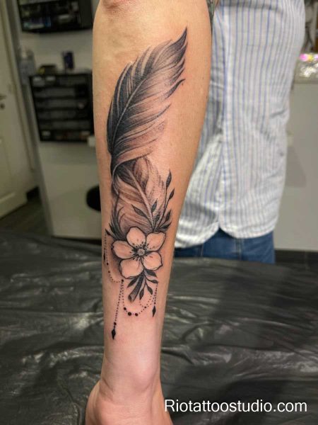 Black and gray feather tattoo with flower and bead details on forearm, realistic feather tattoo ideas