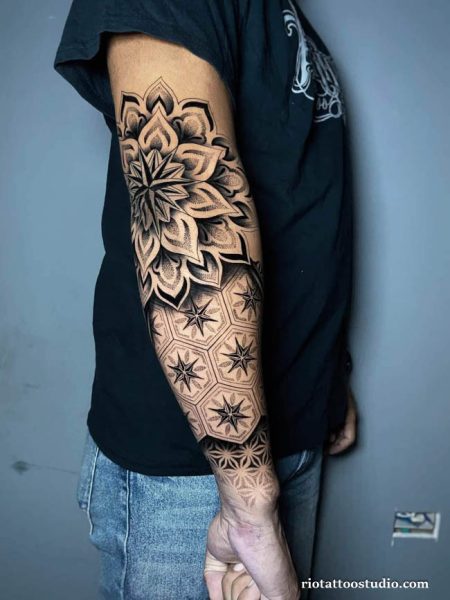 Black and grey half sleeve tattoo with large mandala flower and geometric star patterns on upper arm and forearm