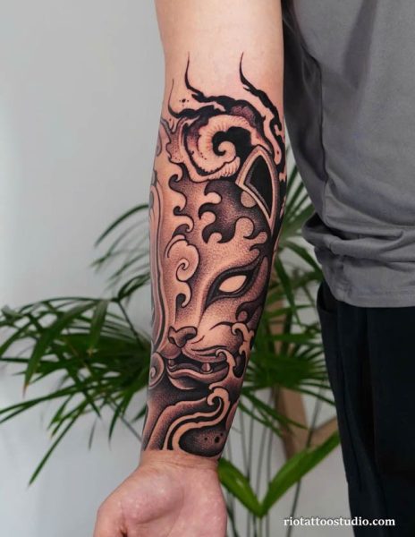 Black and grey oni mask half sleeve tattoo with swirling smoke and bold lines on forearm