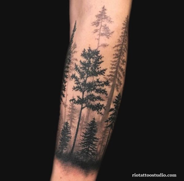 Minimalist forest half sleeve tattoo with tall pine trees and atmospheric shading on forearm
