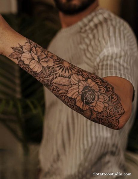 Black and grey floral half sleeve tattoo with large peonies and geometric patterns on forearm and elbow