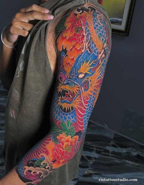 Vibrant Japanese dragon tattoo with blue head, orange mane and red peonies in full color on shoulder and arm, japanese dragon tattoo ideas