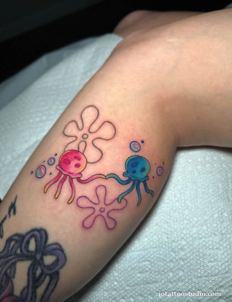 Cute colorful cartoon jellyfish tattoo with pink and blue jellyfish holding tentacles and flowers on arm, jellyfish tattoo ideas