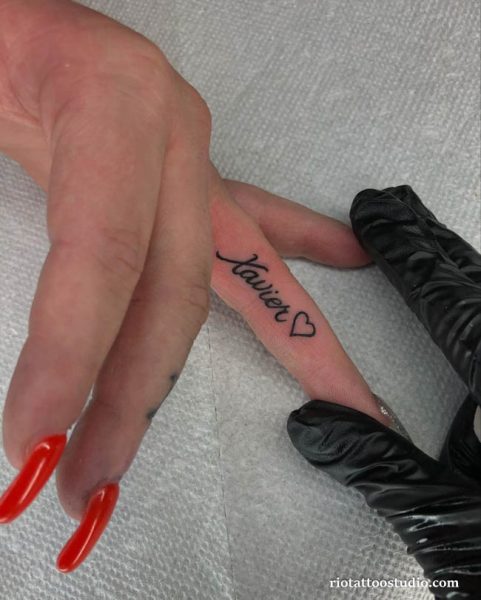 Small name tattoo "Xavier" in cursive script with tiny heart on finger, name tattoo ideas