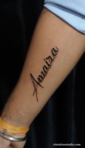Elegant cursive name tattoo "Amaira" in black script on forearm, name tattoo ideas